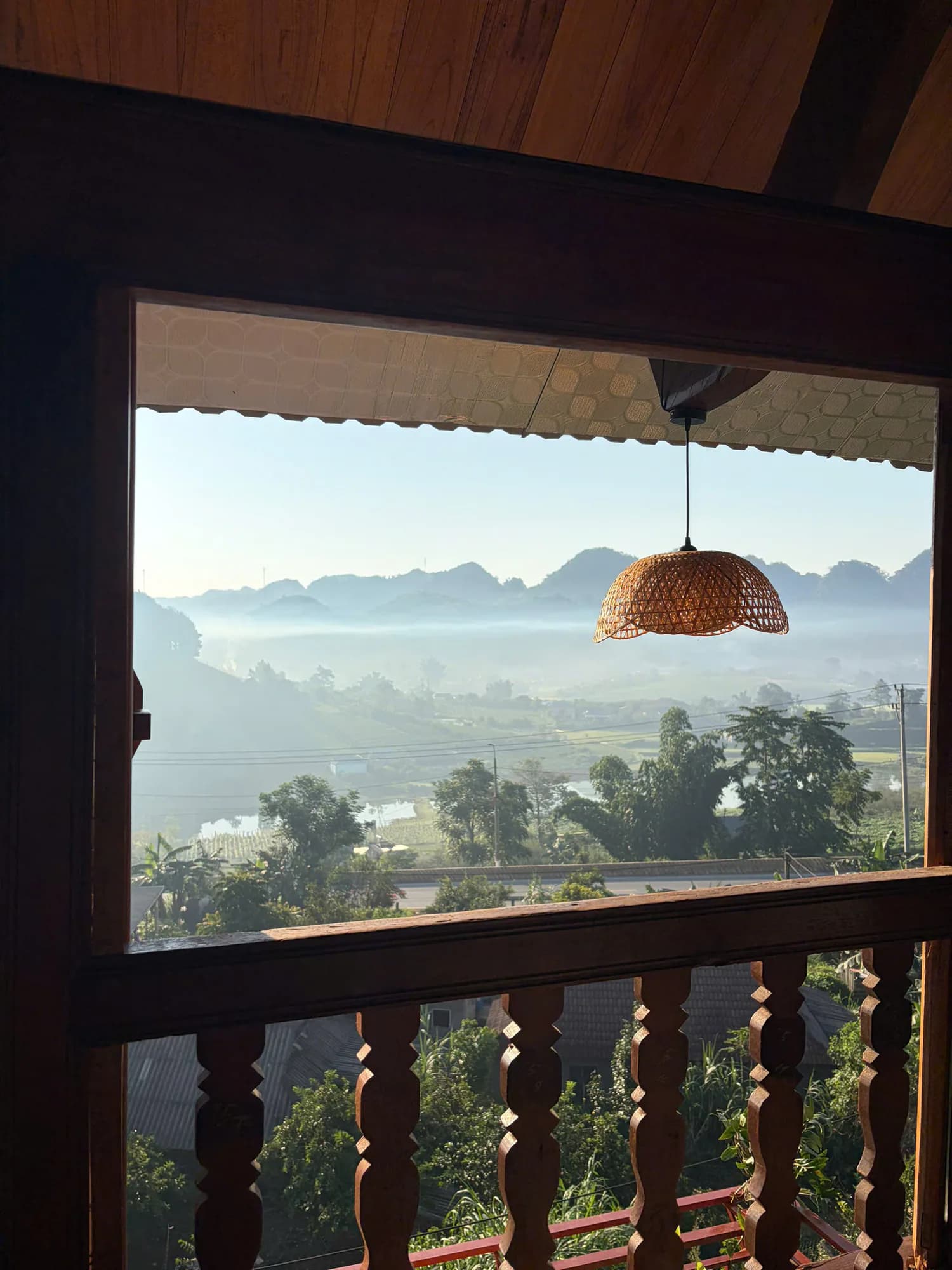 Núi đá phủ sương qua ô cửa và lan can gỗ phòng C1